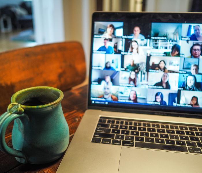 Coffe mug next to laptop with Zoom showing faces blurred out on a video meeting