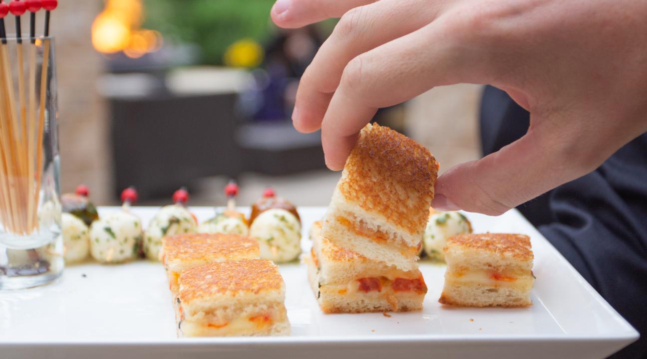 Hand grabbing a mini sandwich on a plate 