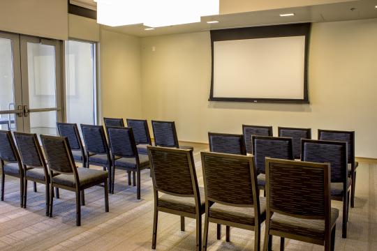 a room with light green walls, with rows of chairs oriented towards a projector screen