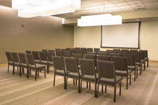 a room with light green walls, with rows of chairs oriented towards a projector screen