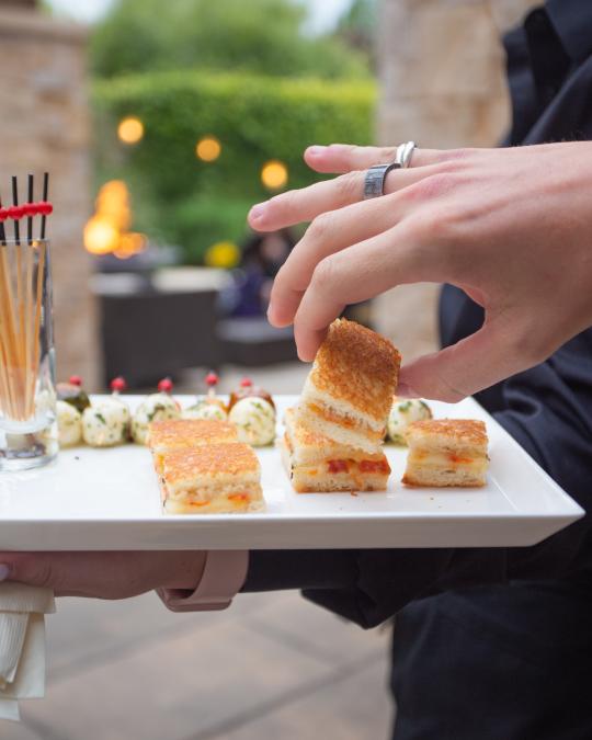 Hand grabbing a mini sandwich on a plate 