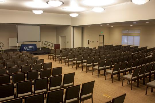 an interior of a meeting space with large screen and many dark chairs