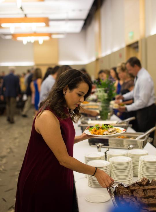 Person holding plate of food and grabbing more food with tongs 