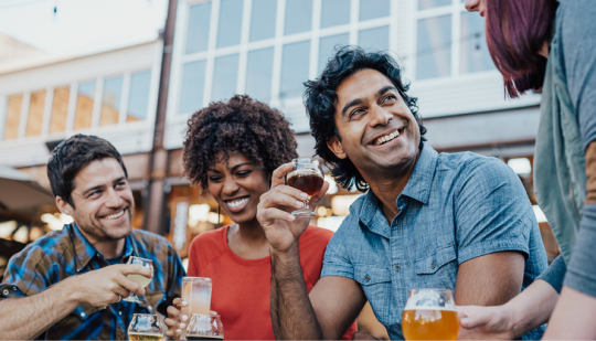 four adults sitting together drinking wine and beer