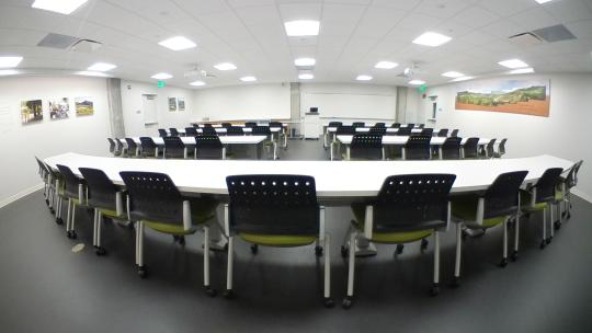 a meeting space with white walls and rows of long white tables with black chairs