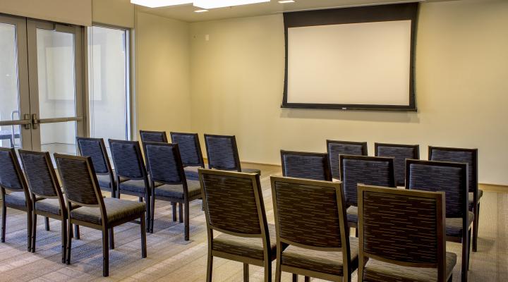 a room with light green walls, with rows of chairs oriented towards a projector screen