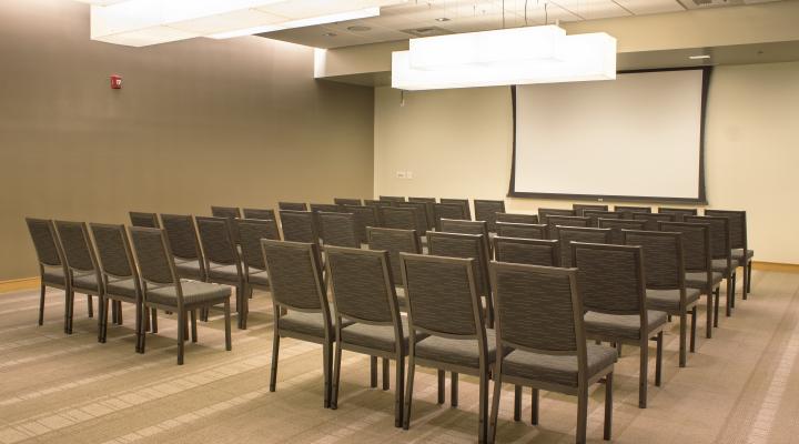 a room with light green walls, with rows of chairs oriented towards a projector screen